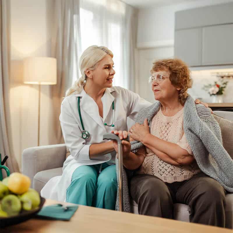 Opiekunka medyczna wspiera starszą kobietę w domowym salonie – codzienna profesjonalna opieka w domu opieki dla seniorów