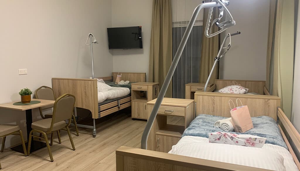Pokój dwuosobowy w domu seniora - jasne, przestronne wnętrze z łóżkami rehabilitacyjnymi i podnośnikiem sufitowym